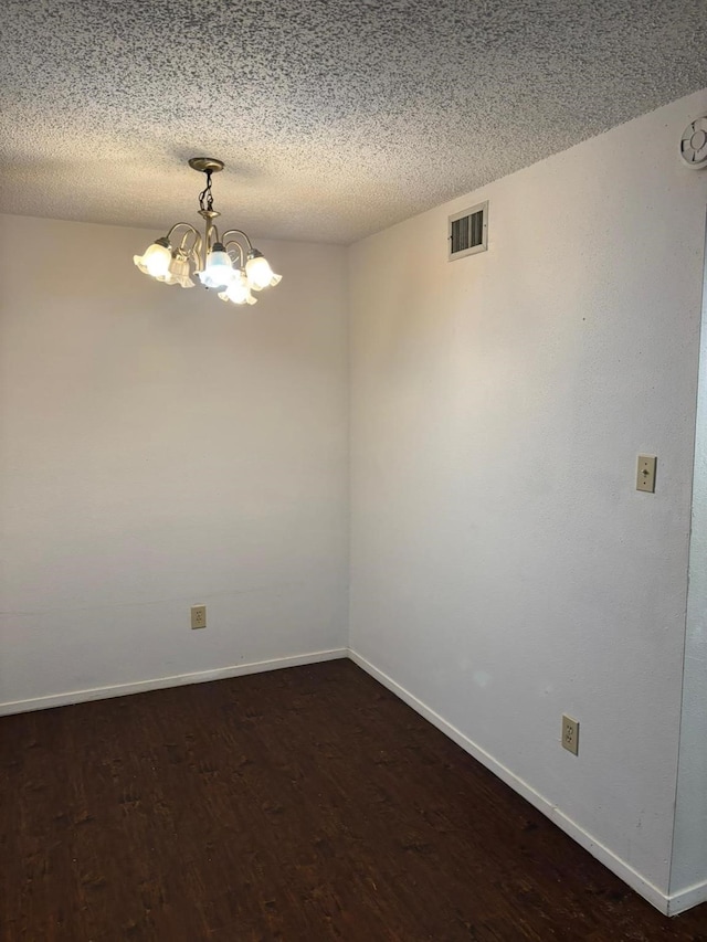 empty room featuring a textured ceiling, dark hardwood / wood-style floors, and a chandelier