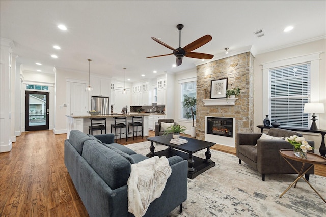 living room featuring ceiling fan, ornamental molding, a stone fireplace, and light hardwood / wood-style floors