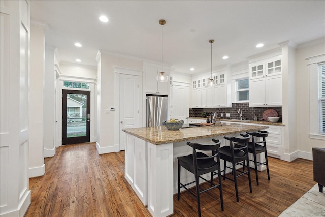 kitchen featuring stainless steel refrigerator, light stone countertops, a center island with sink, and white cabinets