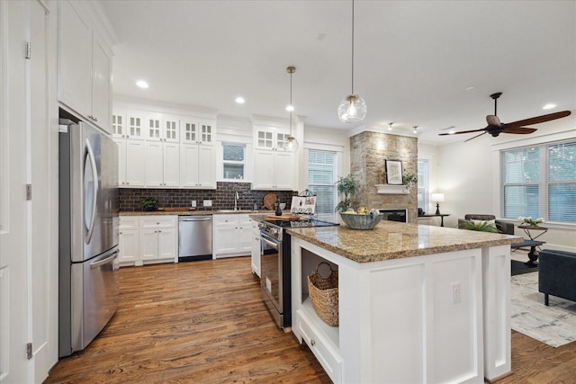 kitchen featuring appliances with stainless steel finishes, white cabinetry, hanging light fixtures, a center island, and light stone countertops