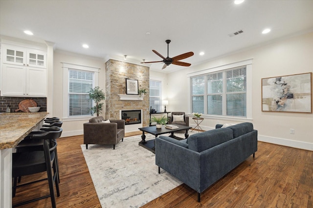 living room with crown molding, ceiling fan, dark hardwood / wood-style floors, and a stone fireplace