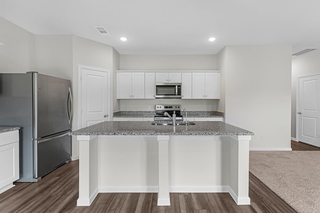 kitchen with appliances with stainless steel finishes, stone countertops, sink, white cabinets, and a center island with sink