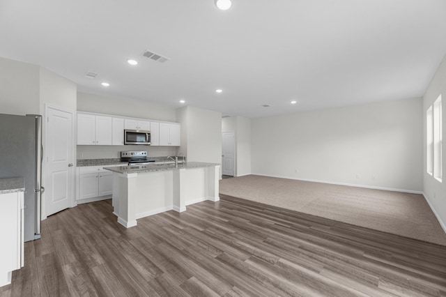 kitchen featuring hardwood / wood-style flooring, white cabinetry, stainless steel appliances, light stone counters, and an island with sink