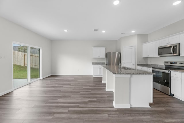 kitchen with white cabinetry, appliances with stainless steel finishes, a kitchen island with sink, and dark stone counters