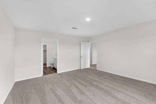 unfurnished bedroom featuring connected bathroom, a spacious closet, and dark colored carpet