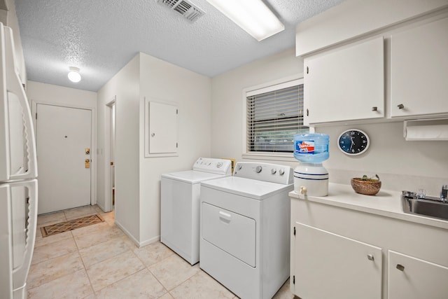 clothes washing area with light tile patterned flooring, sink, cabinets, washer and clothes dryer, and a textured ceiling