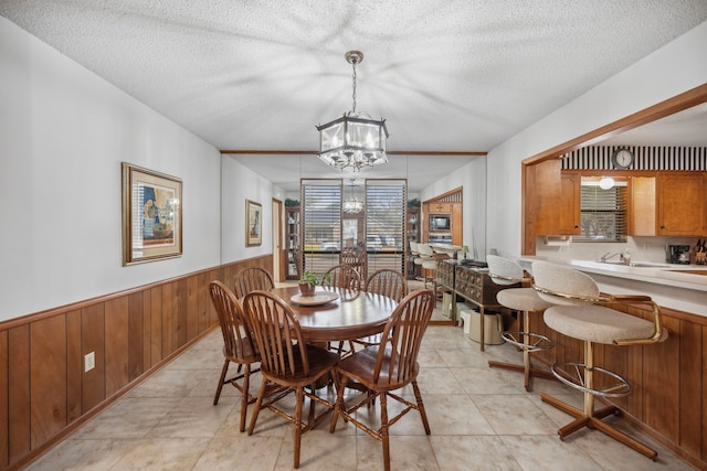 dining room with an inviting chandelier, a textured ceiling, and wood walls