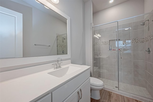 bathroom with vanity, toilet, a shower with shower door, and hardwood / wood-style floors