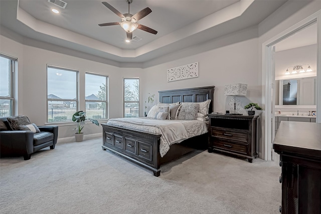 bedroom featuring ensuite bathroom, a tray ceiling, and light carpet