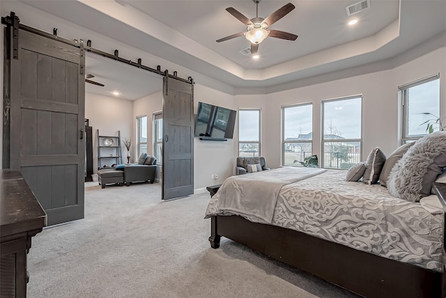 carpeted bedroom featuring a barn door, a raised ceiling, and multiple windows