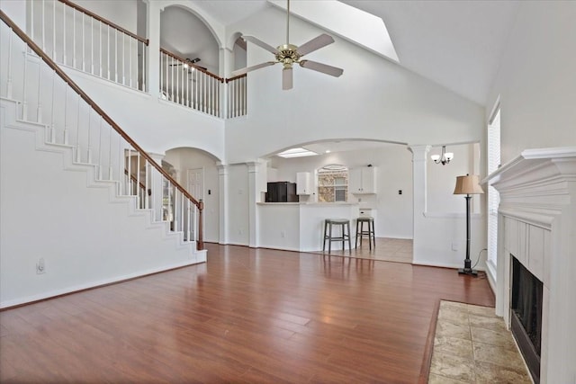 unfurnished living room featuring ornate columns, a tile fireplace, a towering ceiling, hardwood / wood-style flooring, and ceiling fan