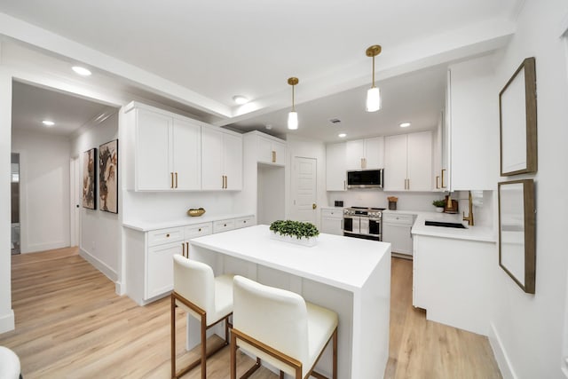 kitchen featuring a kitchen island, appliances with stainless steel finishes, decorative light fixtures, white cabinetry, and light hardwood / wood-style flooring