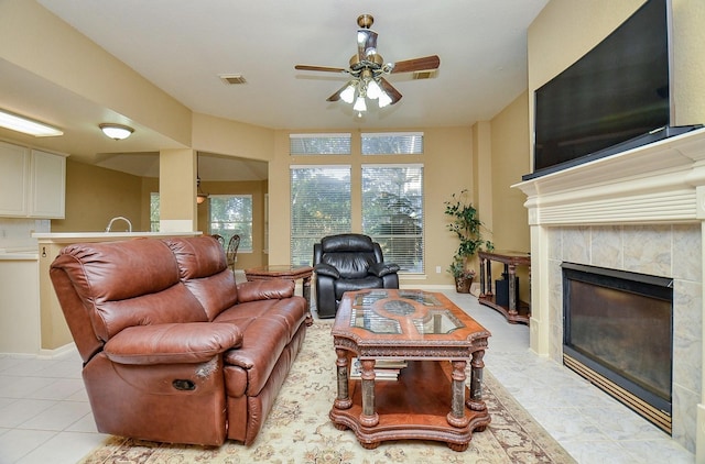 tiled living room with a tile fireplace and ceiling fan