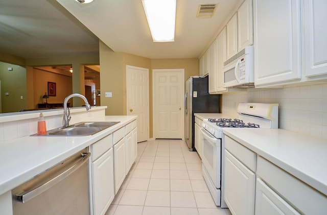 kitchen with sink, light tile patterned floors, appliances with stainless steel finishes, white cabinetry, and backsplash