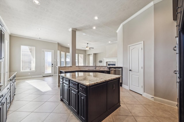 kitchen with sink, ceiling fan, a center island, light stone counters, and a stone fireplace