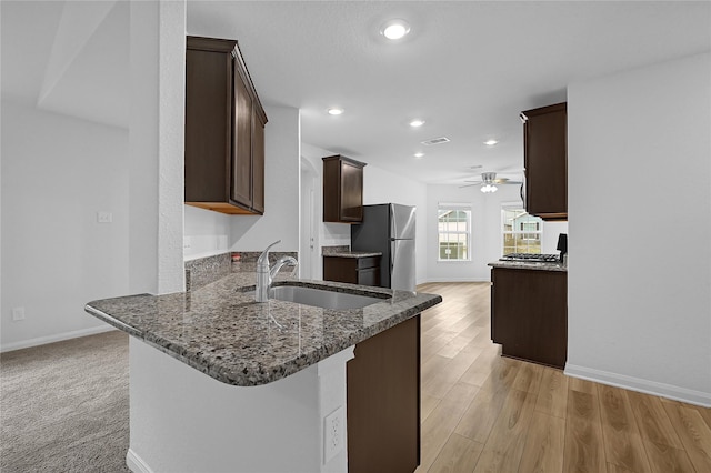 kitchen with sink, stainless steel fridge, dark stone counters, light hardwood / wood-style floors, and kitchen peninsula