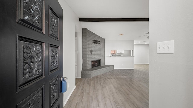 living room featuring a brick fireplace, vaulted ceiling with beams, ceiling fan, and light wood-type flooring