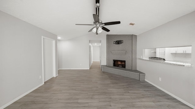 unfurnished living room with lofted ceiling, a fireplace, ceiling fan, and light hardwood / wood-style flooring