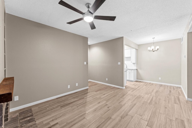 unfurnished living room with ceiling fan with notable chandelier, a textured ceiling, and light wood-type flooring