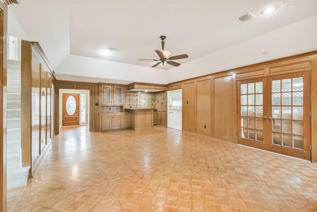 unfurnished living room with french doors, vaulted ceiling, wooden walls, ceiling fan, and light parquet flooring