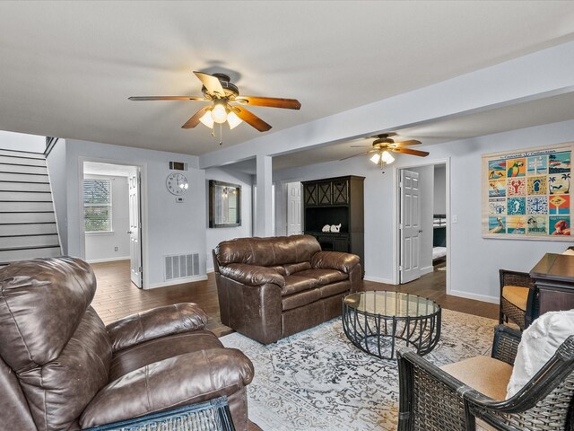 living area featuring ceiling fan, stairs, visible vents, and wood finished floors