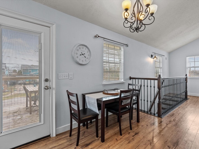 dining area featuring a textured ceiling, lofted ceiling, a notable chandelier, wood finished floors, and baseboards