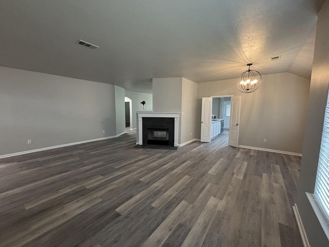 unfurnished living room featuring vaulted ceiling, dark hardwood / wood-style floors, a textured ceiling, and an inviting chandelier