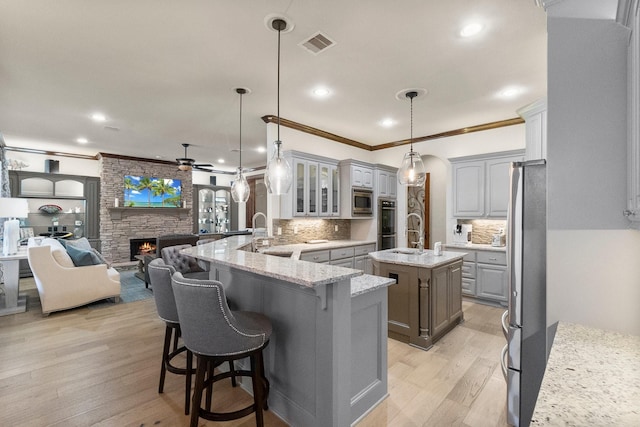 kitchen featuring gray cabinetry, hanging light fixtures, kitchen peninsula, stainless steel appliances, and a kitchen island with sink