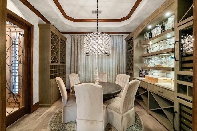 wine area featuring ornamental molding, a raised ceiling, and light hardwood / wood-style floors