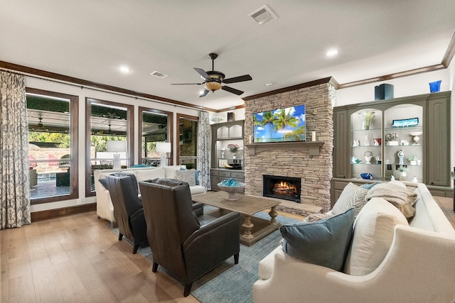 living room with crown molding, built in features, ceiling fan, a fireplace, and light wood-type flooring