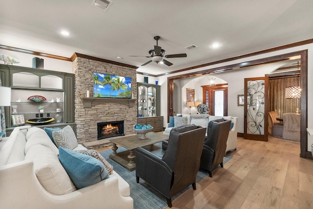 living room featuring a fireplace, light hardwood / wood-style flooring, ornamental molding, and ceiling fan