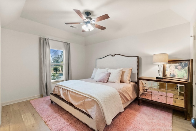 bedroom with a raised ceiling, ceiling fan, and light hardwood / wood-style flooring