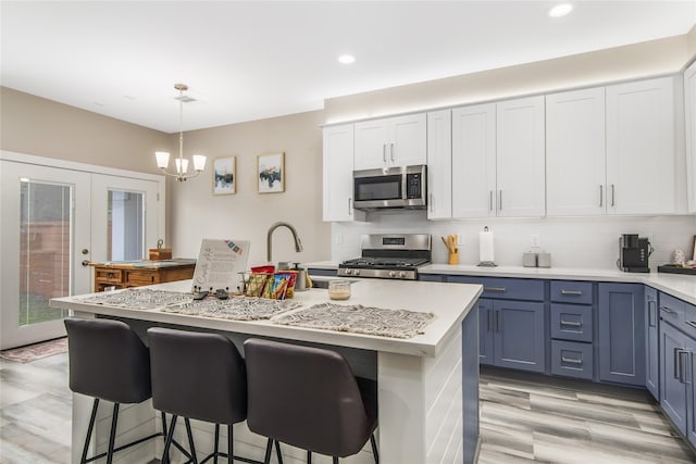 kitchen featuring white cabinetry, hanging light fixtures, an island with sink, and appliances with stainless steel finishes