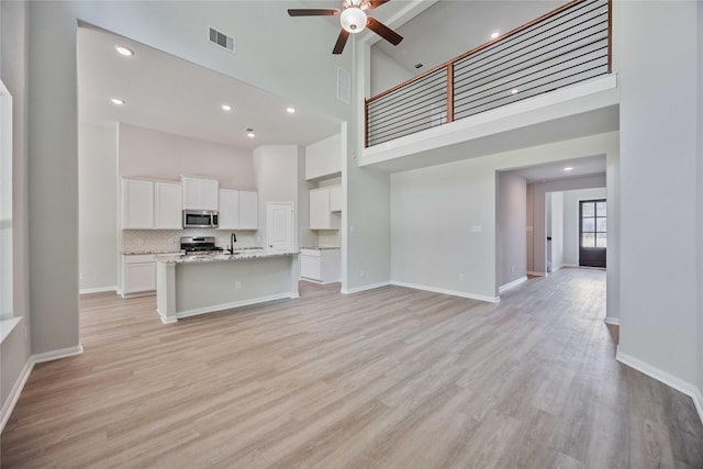 kitchen with white cabinets, a center island with sink, a high ceiling, and appliances with stainless steel finishes