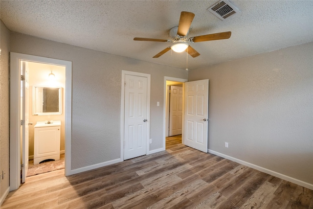 unfurnished bedroom with connected bathroom, sink, a textured ceiling, hardwood / wood-style flooring, and ceiling fan