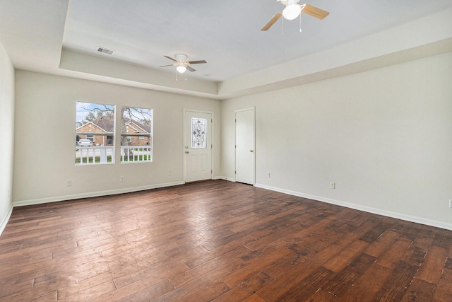 empty room with ceiling fan, dark hardwood / wood-style flooring, and a tray ceiling