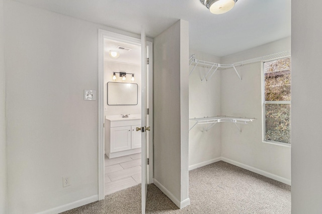 walk in closet with light colored carpet and sink