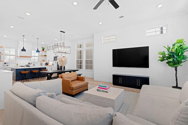 living room with crown molding, ceiling fan with notable chandelier, and light hardwood / wood-style flooring