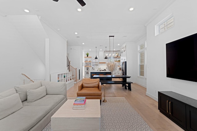 living room with crown molding, light hardwood / wood-style flooring, and ceiling fan with notable chandelier