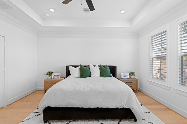 bedroom with crown molding, a tray ceiling, light hardwood / wood-style floors, and ceiling fan