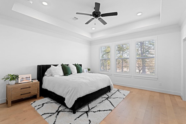 bedroom with light hardwood / wood-style flooring, ceiling fan, and a tray ceiling