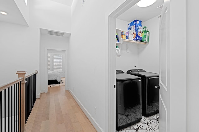 clothes washing area featuring washing machine and clothes dryer and light wood-type flooring