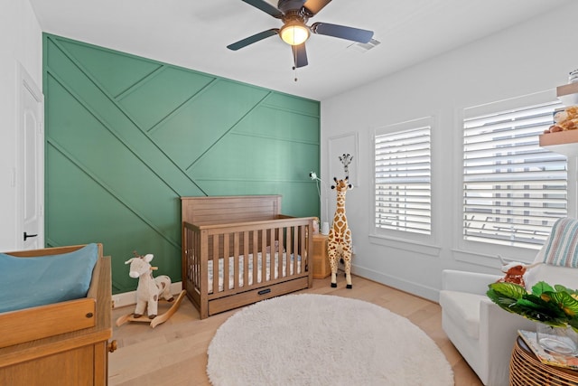 bedroom featuring a crib, light hardwood / wood-style floors, and ceiling fan