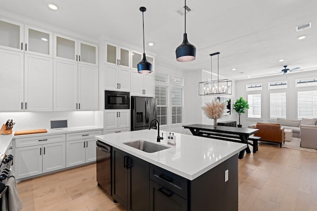 kitchen with sink, black appliances, hanging light fixtures, an island with sink, and white cabinets