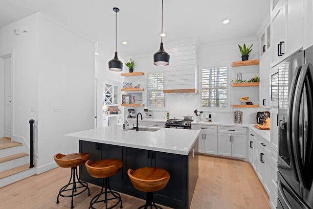 kitchen featuring sink, white cabinetry, a kitchen island with sink, stainless steel range with gas stovetop, and black refrigerator with ice dispenser