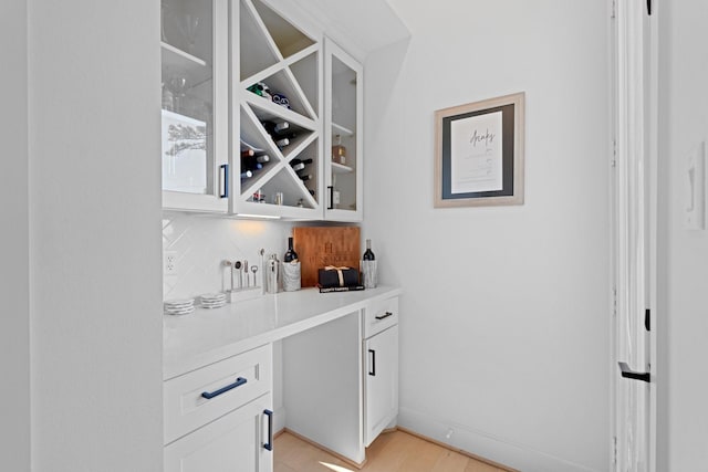 bar with white cabinetry, light hardwood / wood-style floors, and decorative backsplash