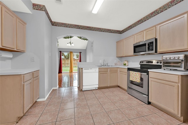 kitchen with light tile patterned flooring, light brown cabinetry, sink, appliances with stainless steel finishes, and a notable chandelier