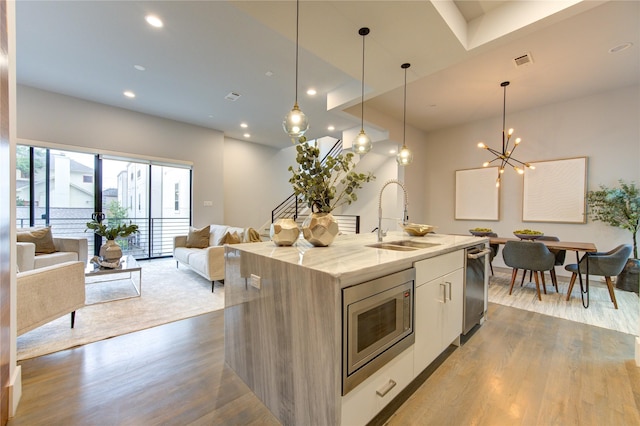 kitchen with sink, decorative light fixtures, an island with sink, stainless steel appliances, and light stone countertops