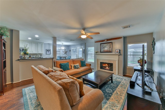 living room featuring a tile fireplace, a healthy amount of sunlight, dark wood-type flooring, and ceiling fan