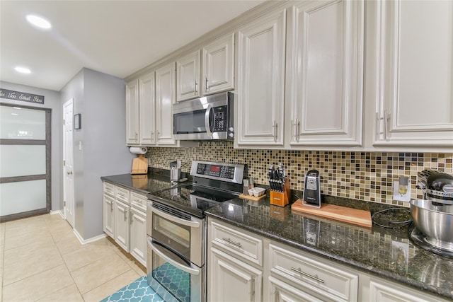 kitchen with white cabinets, backsplash, dark stone counters, light tile patterned floors, and stainless steel appliances